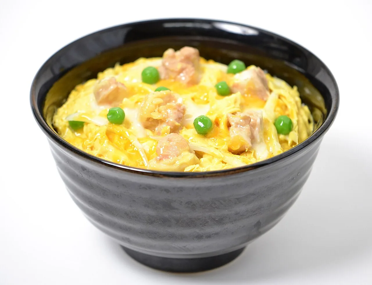 A black bowl of oyakodon topped with chicken, soft egg, onion, and green peas.